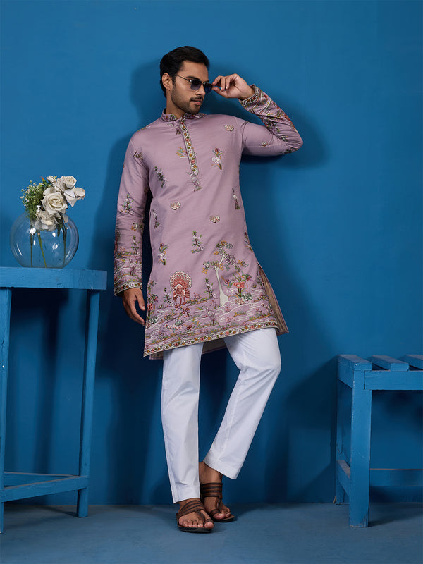 Man wearing a pink embroidered kurta with white pants against a blue background
