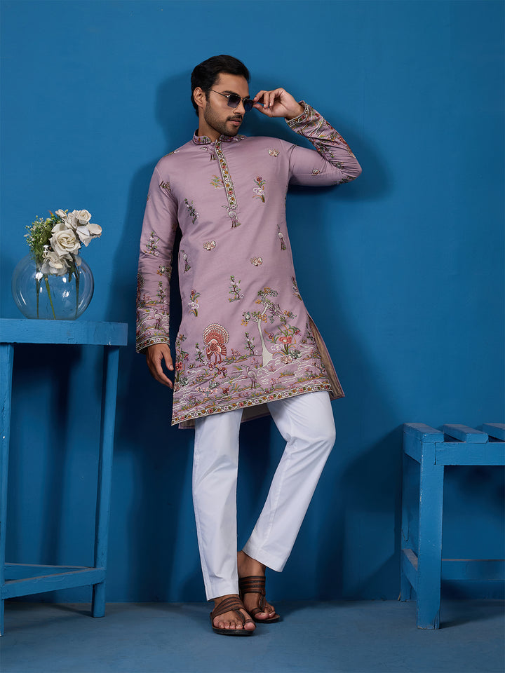 Man wearing a pink embroidered kurta with white pants against a blue background