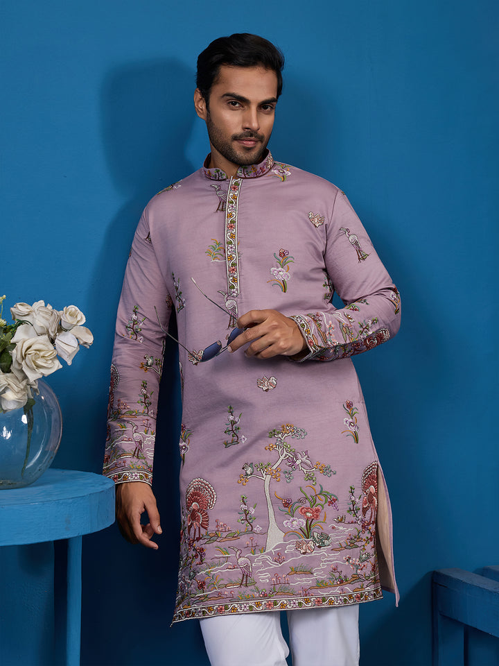 Man wearing a pink embroidered kurta with white pants against a blue background