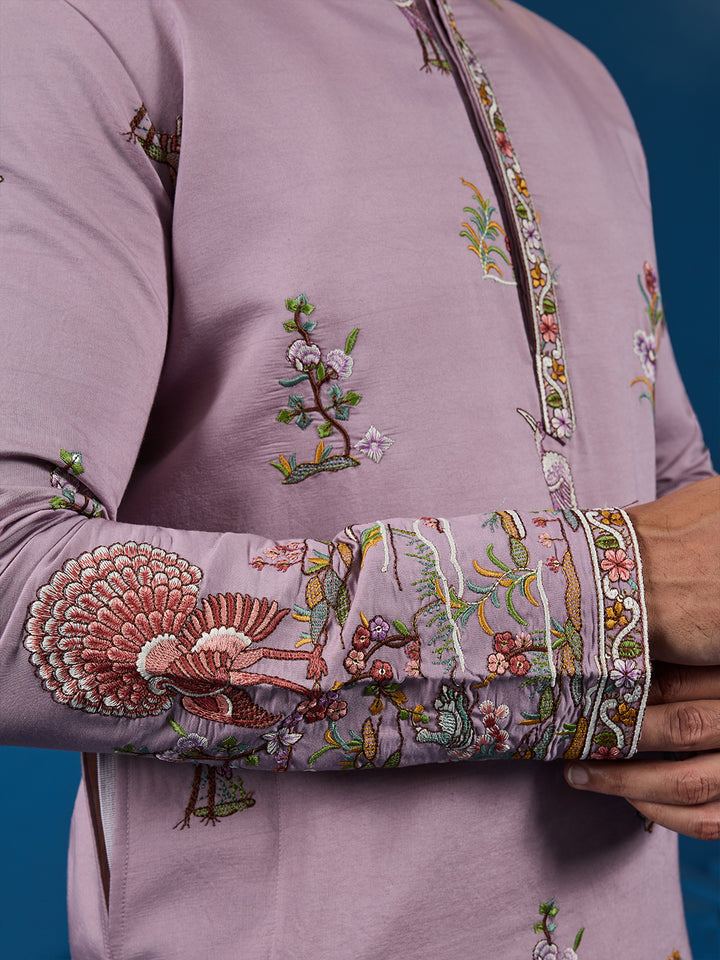 Close-up of a mauve traditional outfit with intricate floral and bird embroidery on a blue background