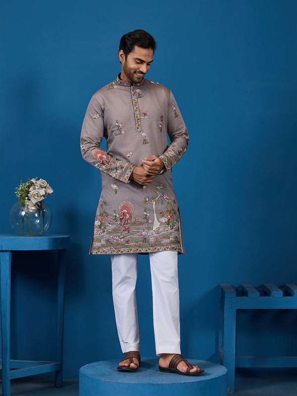 Man wearing a traditional embroidered kurta with white pants against a blue background
